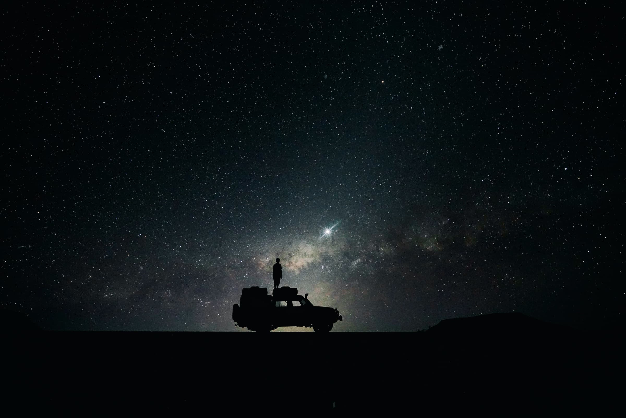 A silhouetted figure standing on a truck under the Milky Way